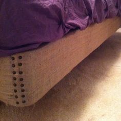 an unmade bed with purple sheets and buttons on the headboard is seen in this image