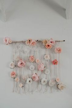 an arrangement of flowers hanging on a white wall with sticks and string attached to it