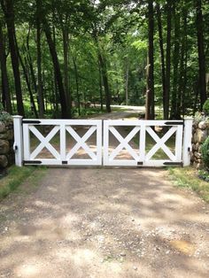 a white gate in the middle of a dirt road surrounded by trees and rocks on both sides