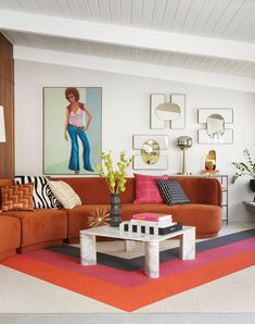 a living room with orange couches and colorful rugs on the floor in front of a painting