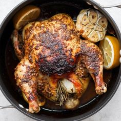 a roasted chicken in a pot with lemons and garlic