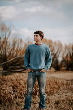 a young man standing in a field with his hands on his hips and looking off into the distance