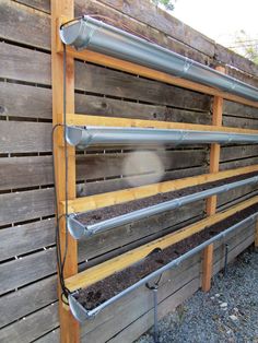 a wooden fence with metal pipes attached to it and some dirt in the ground below