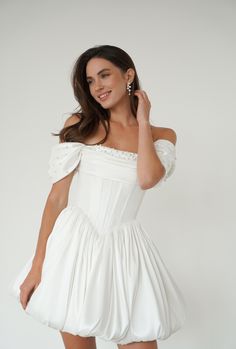 a woman in a white dress posing for the camera with her hand on her shoulder