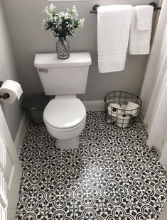 a white toilet sitting in a bathroom next to a sink and towel rack on top of a tiled floor