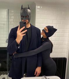 a man in a batman mask takes a selfie with a woman in a bathroom