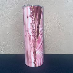 a pink marbled vase sitting on top of a black table next to a white wall