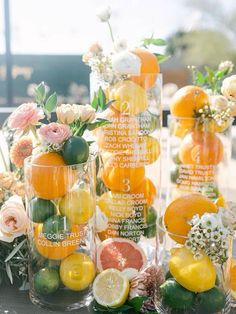 an arrangement of citrus fruits and flowers in vases on a table with other fruit