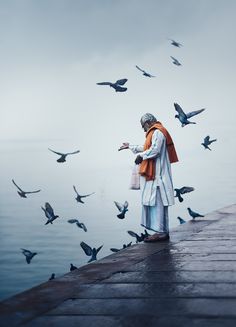 a man standing on a dock surrounded by birds flying over the water in front of him