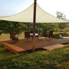 a deck with chairs and an awning over it in the middle of a field