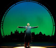 a man standing on top of a stage in front of a green screen with his arms outstretched