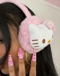 a woman with long black hair and pink nail polish holding up a hello kitty headphone