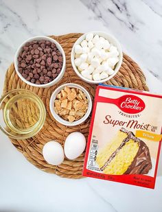 ingredients to make a cake sitting on a wicker tray, including eggs, marshmallows, and chocolate