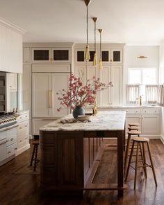 a kitchen with wooden floors and white cabinets, marble counter tops, and bar stools