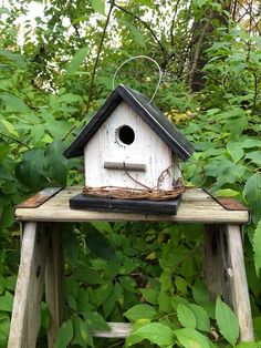 a bird house sitting on top of a wooden table in the middle of some trees