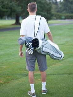 a man carrying golf equipment on a green field