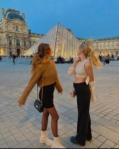 two women standing in front of the pyramid at night, one is talking on her cell phone