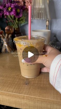 a person is holding a drink with a pink straw in it on a wooden table