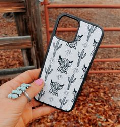 a person holding up a phone case with cactus and bull heads on it in front of a fence