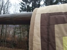 the back end of a bench with a quilted seat cover on it and trees in the background