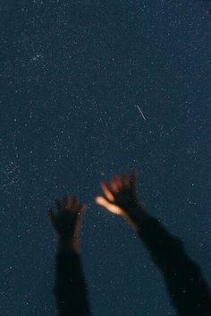 two hands reaching up at the stars in the night sky with their arms extended out