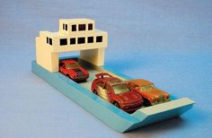 two toy cars are parked in front of a model house on a boat that is built into the water