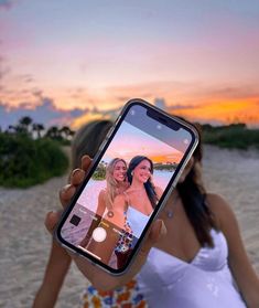 a woman taking a selfie with her cell phone on the beach at sunset or sunrise