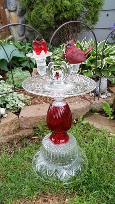 two glass candlesticks sitting on top of a cake plate in the grass next to a garden