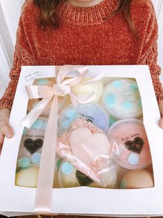 a woman holding a box with cupcakes in it and a bow on the front