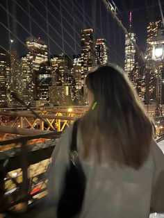 a woman standing on top of a bridge looking at the city lights in the distance