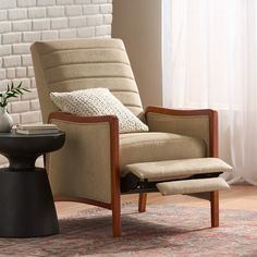 a chair and ottoman in front of a brick wall with a vase on the side table