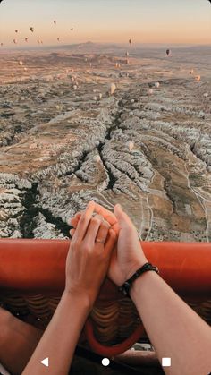 two people holding hands while looking at hot air balloons in the sky