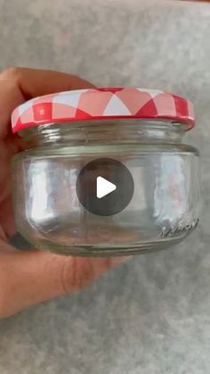 a hand holding a glass jar with a red and white cover on it's lid