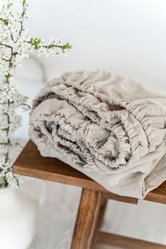 a stack of blankets sitting on top of a wooden table next to a vase with flowers