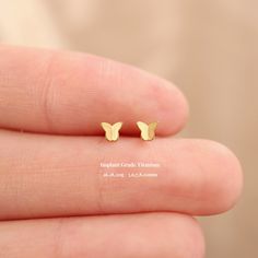 small gold butterfly stud earrings on someone's finger