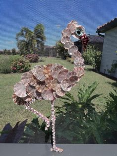 a metal flamingo sculpture sitting on top of a lush green field next to a house