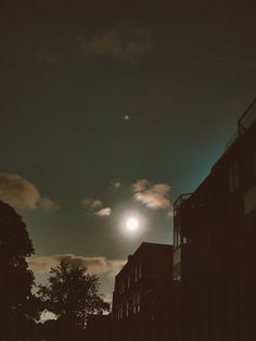 the moon is shining brightly in the sky above some buildings and trees at night time