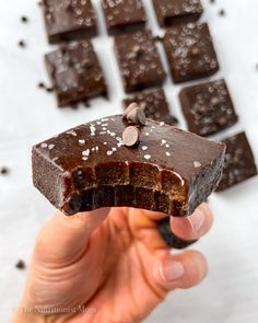 a hand holding up a piece of chocolate with sea salt on top and pieces of dark chocolate in the background