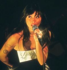 a woman holding a microphone in her right hand and wearing a white shirt with writing on it