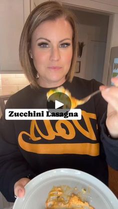 a woman holding a fork in her hand while eating food from a plate with the words zucchini lasagna on it