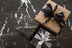 two wrapped gift boxes with black and white bows on them sitting on a marble surface