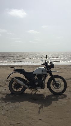 a motorcycle is parked on the beach near the water's edge and waves are in the background