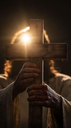 a person holding a wooden cross in front of a light shining through the darkness with their hands