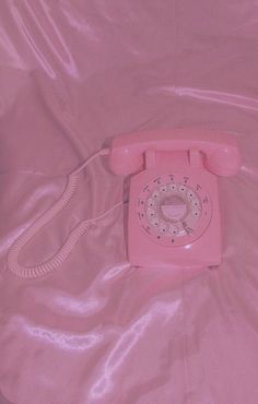 an old pink phone laying on top of a pink sheeted bed with the cord still attached