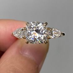 a diamond ring with three pear shaped diamonds on it's side, in someones hand