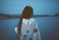 a woman with long hair standing in front of water