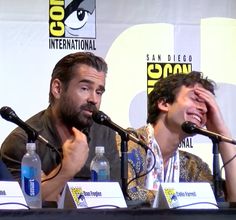 two men sitting at a table with microphones in front of them and one man holding his head