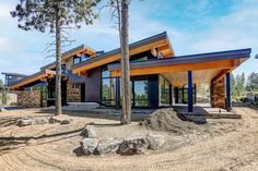 a modern house with lots of windows in the middle of trees and dirt on the ground