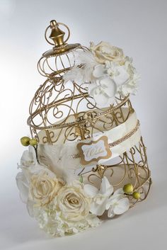 a gold and white wedding cake with flowers on the top is adorned with an elaborate birdcage