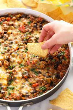 a person dipping a tortilla chip into a skillet filled with mexican food